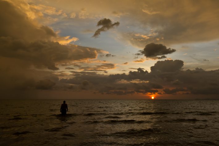 At Otres Beach in Cambodia, a man wades out to sea as the sun casts its final rays over the ocean.